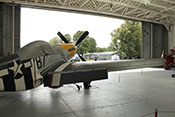 Blick über die rechte Tragfläche der P-51D 'Ferocious Frankie' durch das geöffnete Tor eines historischen RAF-Hangars 
